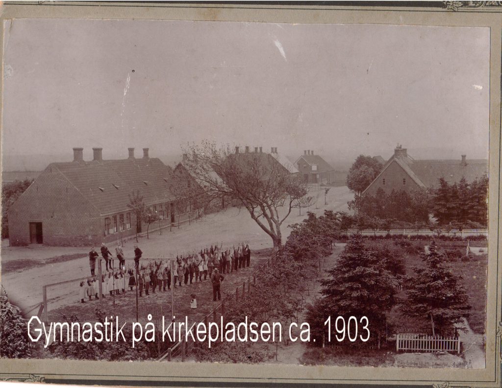 Førstelærer Thomas Thomasen havde i 1895 gymnastik med eleverne. på kirrkepladsen umiddelbart ved siden af det gamle træ. Måske har det været en kdd omgang. På den anden side af vejen ligger den skole, som blev bygget iu 1840.