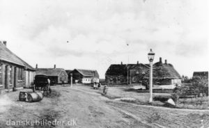 Sådan så kirkepladsen i Ørre ud i 1906. Man bemærker den markante gaslampe og bagved ligger skolen, som nu er kirkehus. Til højre ses noget af kirken. I gården til venstre i billedet boede den navnkundige skolelærer og foregangsmand Iver Holmgaard.